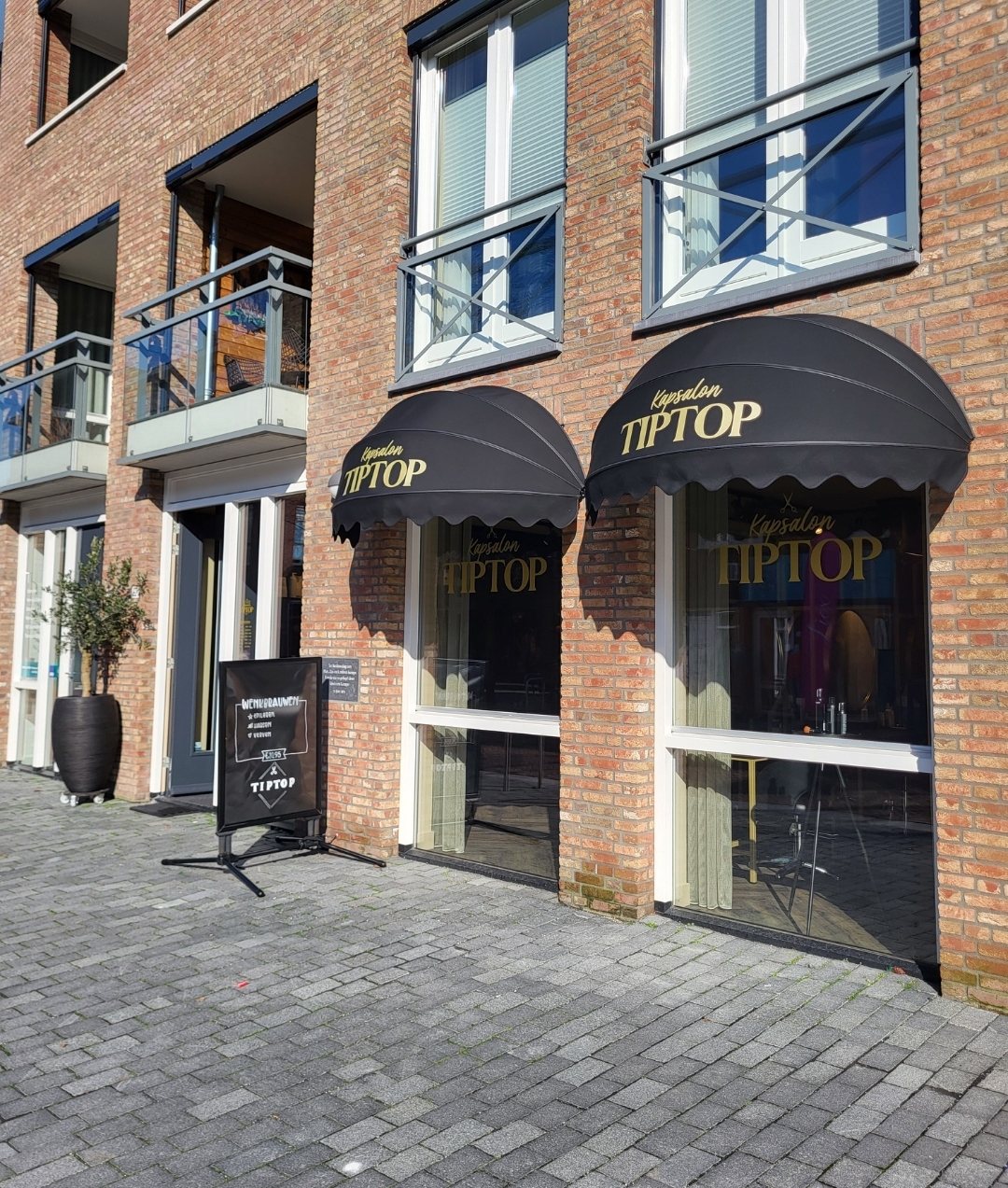De winkelpui aan de Hoofdstraat 92 met zwarte luifels en gouden letters